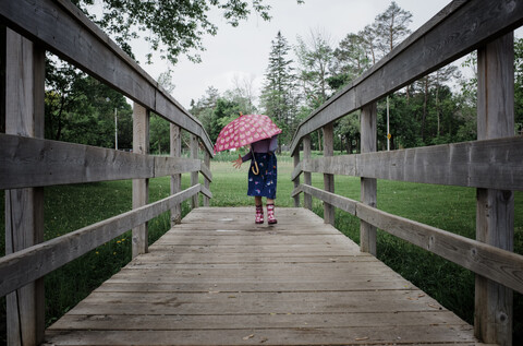 Mädchen mit Regenschirm auf dem Steg im Park während der Regenzeit, lizenzfreies Stockfoto