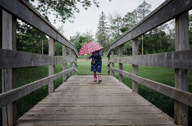 Mädchen mit Regenschirm auf dem Steg im Park während der Regenzeit - CAVF49428