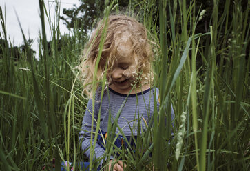 Close-up of happy girl sitting amidst grassy field. - CAVF49429
