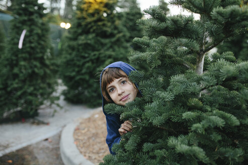 Porträt eines niedlichen Mädchens, das an einem Tannenbaum auf einem Bauernhof steht, während der Weihnachtszeit - CAVF49517