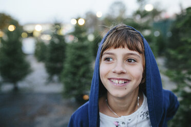 Nahaufnahme eines glücklichen Mädchens, das wegschaut, während es an einem Tannenbaum auf einem Bauernhof in der Weihnachtszeit steht - CAVF49518