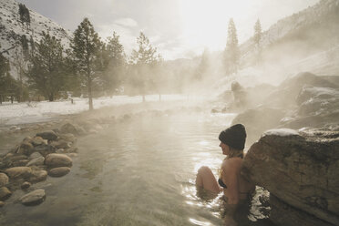 Seitenansicht einer Frau im Bikini, die im Winter in einem Thermalbad im Wald sitzt - CAVF49520