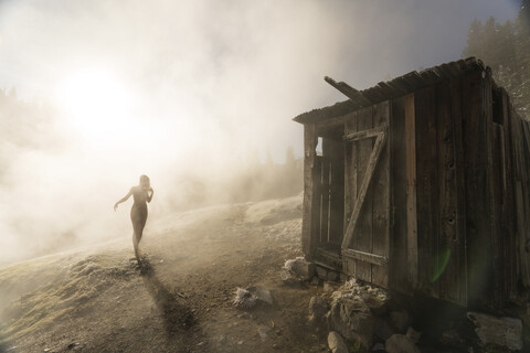 Silhouette woman walking towards old wooden hut on mountain during foggy weather stock photo