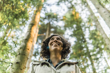 Niedriger Blickwinkel einer glücklichen Frau, die wegschaut, während sie im Wald steht - CAVF49550