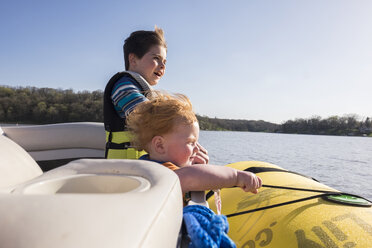 Brüder tragen Schwimmwesten, während sie in einem Boot auf einem See gegen den klaren Himmel an einem sonnigen Tag stehen - CAVF49597