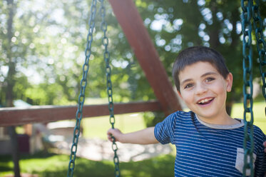 Porträt eines glücklichen Jungen beim Schaukeln im Garten - CAVF49602