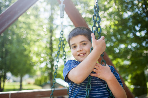 Portrait of happy boy swinging against trees at yard stock photo