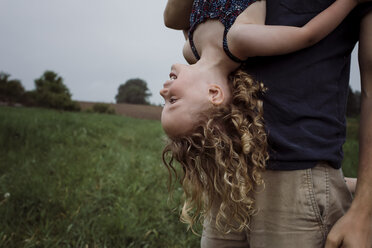 Mittelteil eines Vaters, der seine Tochter auf den Kopf stellt, während er auf einer Wiese vor dem Himmel im Park steht - CAVF49616
