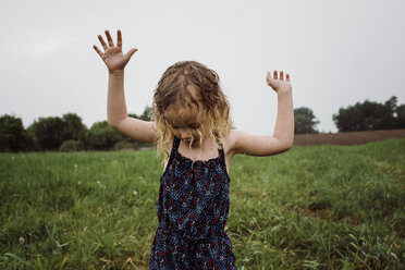 Wet girl with arms raised standing on grassy field against sky at park during rainy season - CAVF49619