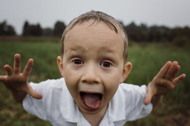 Portrait of wet boy screaming while standing against sky at park during rainy season - CAVF49620
