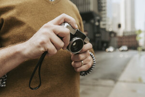 Mittelteil eines Mannes, der eine Kamera hält, während er auf einer Straße in der Stadt steht - CAVF49646
