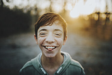 Close-up portrait of happy teenage boy standing outdoors during sunset - CAVF49649