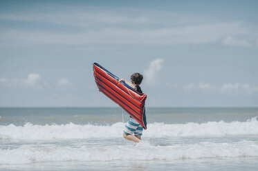 Teenager mit Pool Floß zu Fuß im Meer gegen den Himmel während sonnigen Tag - CAVF49652