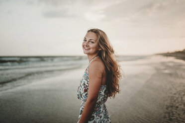 Portrait of happy woman standing at beach against sky during sunset - CAVF49654