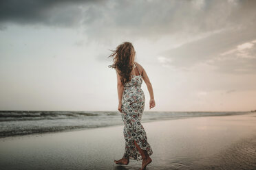 Rückansicht einer am Strand spazierenden Frau gegen den Himmel bei Sonnenuntergang - CAVF49656