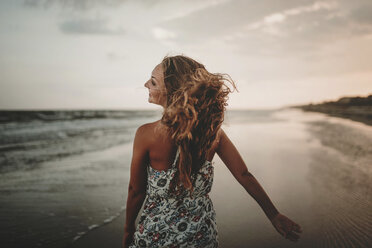 Rückansicht einer glücklichen Frau, die am Strand gegen den Himmel bei Sonnenuntergang spazieren geht - CAVF49657