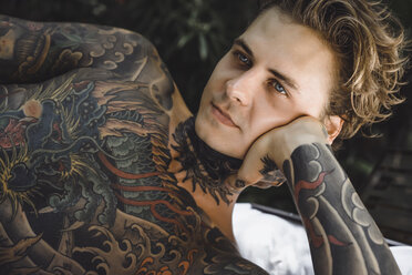 Close-up of thoughtful tattooed man lying on blanket while looking away - CAVF49660
