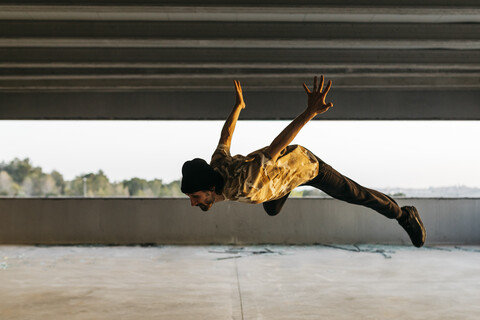 Mann macht Breakdance in städtischem Betongebäude, springt in der Luft, lizenzfreies Stockfoto