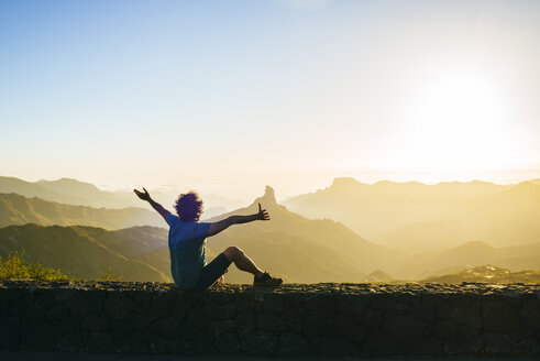 Spain, Canary Islands, Gran Canaria, back view of happy man watching mountain landscape at sunset - KIJF02063