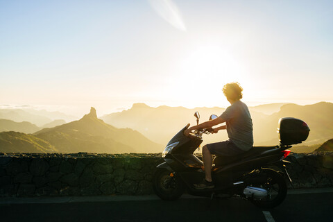 Spain, Canary Islands, Gran Canaria, man on motor scooter watching sunset over mountainscape stock photo