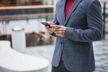 Geschäftsmann in der Lobby eines modernen Gebäudes, mit Smartphone - KKAF02409