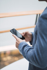 Businessman in lobby of a modern building, using smartphone - KKAF02410