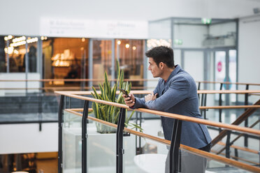 Businessman in lobby of a modern building, using smartphone - KKAF02414