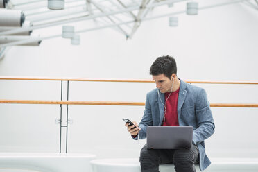 Businessman in lobby of a modern building, using smartphone - KKAF02425