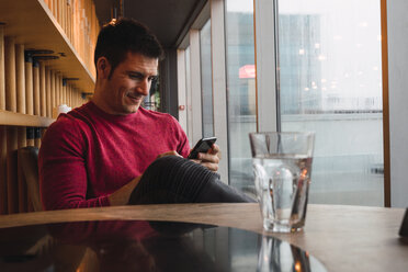 Businessman sitting in restaurant, using his smartphone - KKAF02432