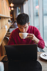 Geschäftsmann sitzt in einem Restaurant mit Laptop und trinkt Kaffee - KKAF02438