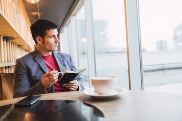 Geschäftsmann sitzt im Restaurant, trinkt Kaffee und schaut in sein Notizbuch - KKAF02440