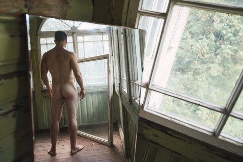 Mirror image of naked man standing at window of abandoned house - KKAF02448