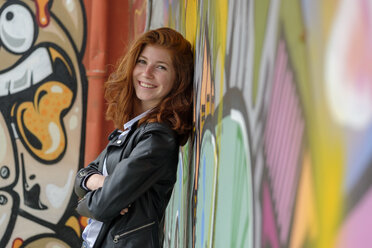 Italy, Finale Ligure, portrait of smiling teenage girl leaning against mural - LBF02124