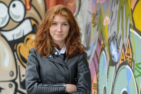 Italy, Finale Ligure, portrait of redheaded teenage girl wearing black leather jacket in front of mural - LBF02125