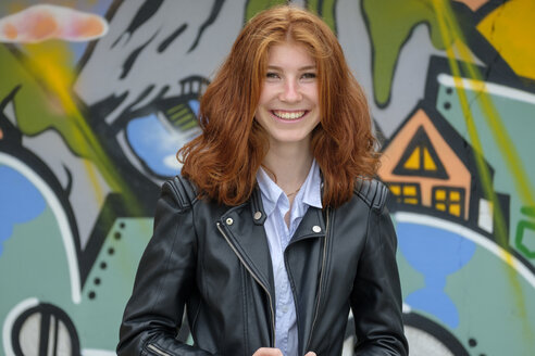 Italy, Finale Ligure, portrait of laughing redheaded teenage girl in front of mural - LBF02126