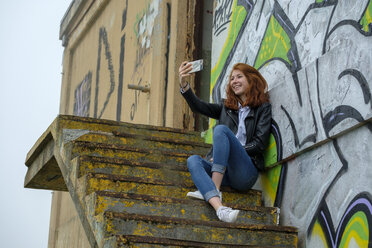 Italien, Finale Ligure, rothaariges Teenager-Mädchen, das ein Selfie vor einer Graffiti-Wand macht - LBF02128