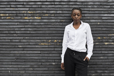 Portrait of smart businesswoman wearing white shirt and black trousers leaning against wall - IGGF00669