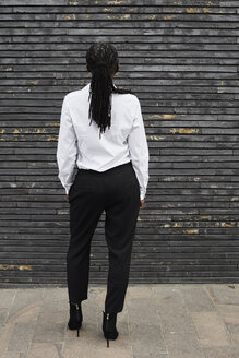 Back view of businesswoman with dreadlocks wearing white shirt and black trousers - IGGF00670