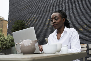 Portrait of smiling businesswoman sitting on terrace of a coffee shop working on laptop - IGGF00680
