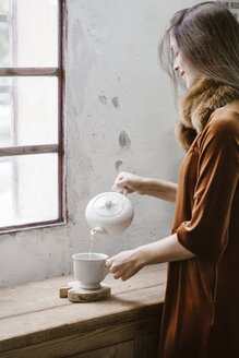 Lächelnde junge Frau gießt Tee in eine Tasse - ALBF00638
