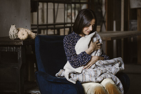 Junge Frau sitzt auf einem Sessel in einem mit einer Decke bedeckten Loft - ALBF00652