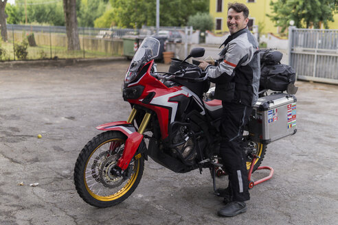 Porträt eines lächelnden Mannes, der sich auf eine Motorradtour vorbereitet - FBAF00126