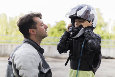 Vater beobachtet Sohn beim Aufsetzen des Motorradhelms - FBAF00127