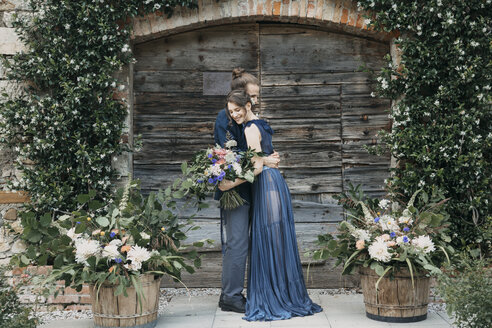 Braut und Bräutigam stehen vor einem Holztor und umarmen sich - ALBF00692