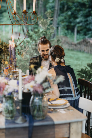 Glückliches Brautpaar sitzt am festlich gedeckten Tisch im Freien, lizenzfreies Stockfoto