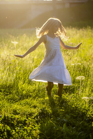 Glückliches Mädchen tanzt auf Sommerwiese im Gegenlicht, lizenzfreies Stockfoto