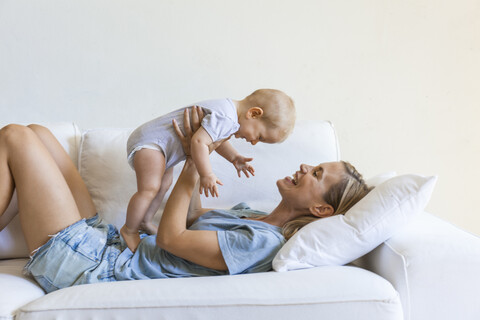 Happy mother lying on couch holding her baby girl stock photo