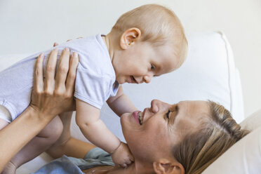 Happy mother lying on couch holding her baby girl - TCF05863