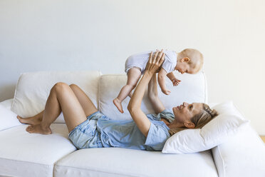 Happy mother lying on couch holding her baby girl - TCF05866