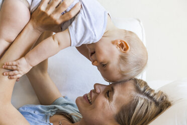 Happy mother cuddling with her baby girl on couch - TCF05868